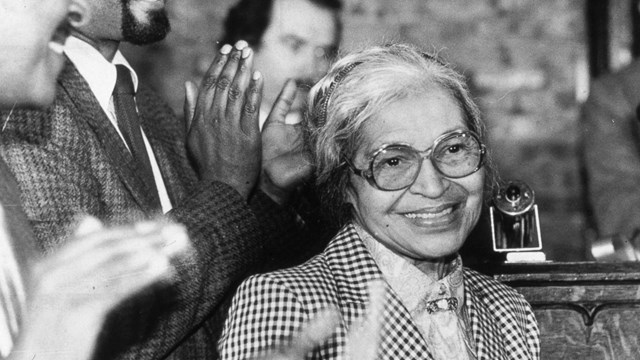 Black and white image of a woman smiling at a camera with hands clapping around her